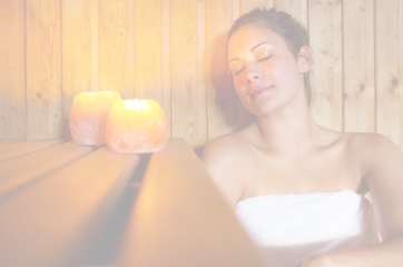 Faded background image of a woman sitting in an infrared sauna with a smile on her face.